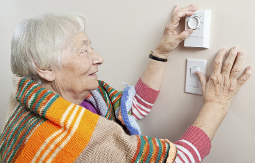 Senior woman saving energy by dressing warm and adjusting her thermostat.
