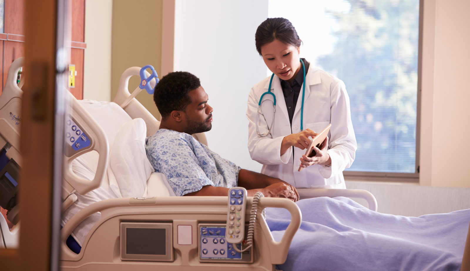 Hospital Doctor With Digital Tablet Talks To Male Patient