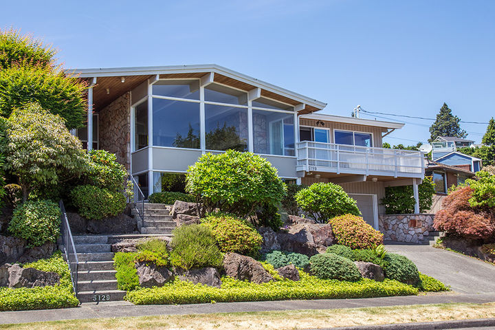 Photo of a home with two flights of stairs to the entrance and a sloping driveway.