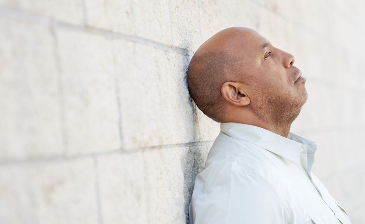 Stressed man leans back against a concrete brick wall