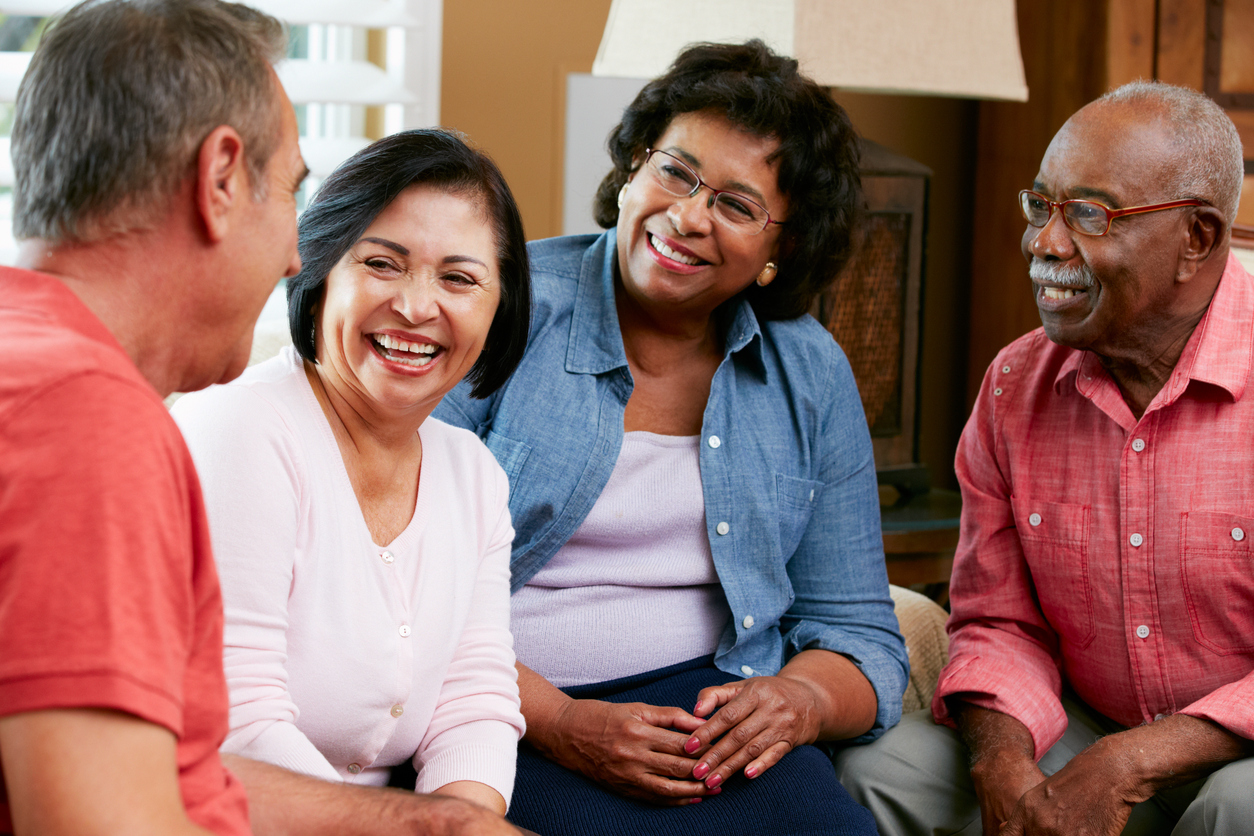 Group of diverse senior friends chatting at home together smiling and enjoying each other's company.