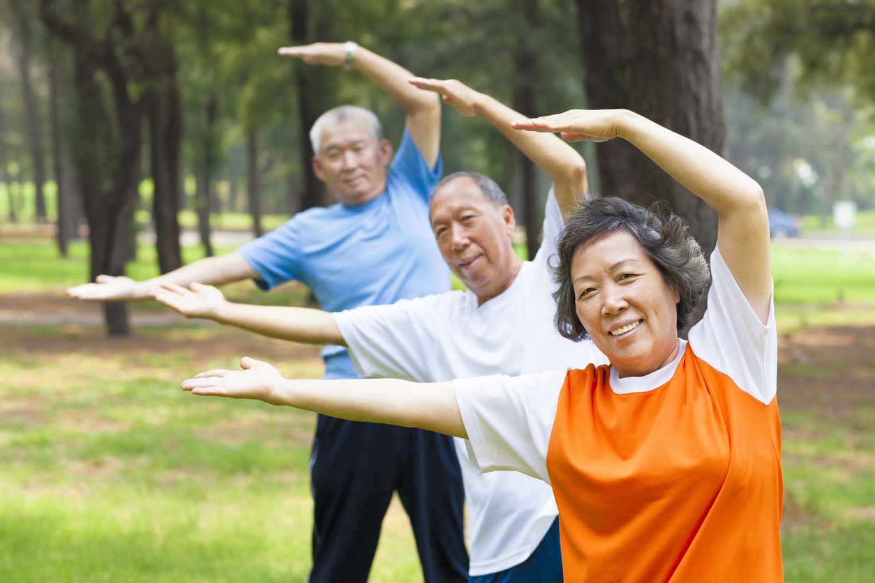 Three asian older adults stretching with arms over head leaning slightly left.