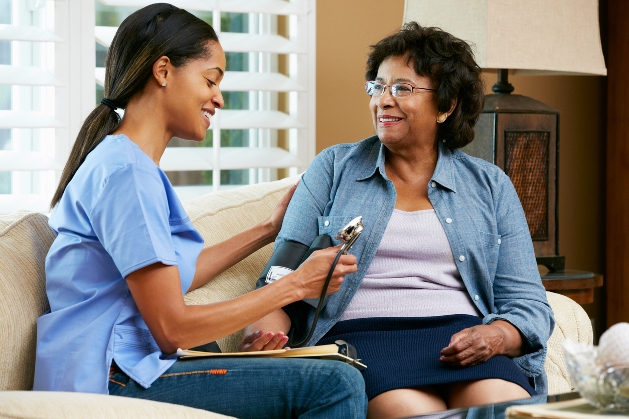 Nurse Visiting Senior Female Patient At Home Taking Blood Pressure Smiling