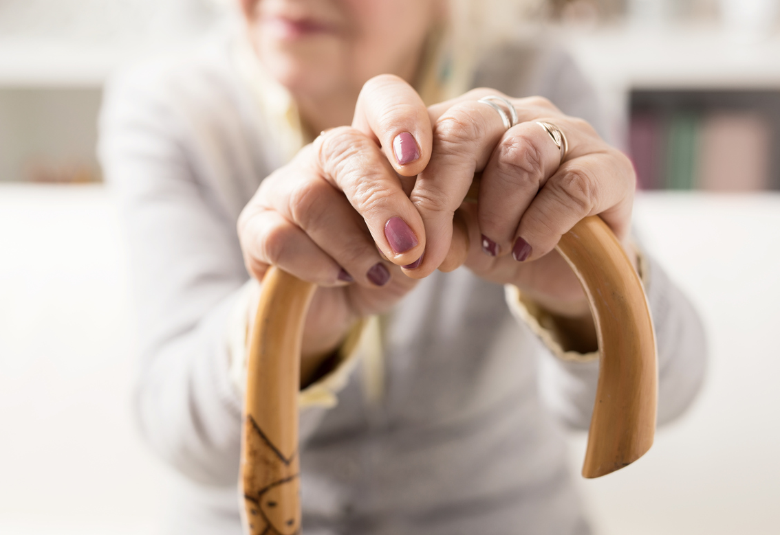Older adult women sitting down with zoom in on her hands holding on to top of wooden cane.