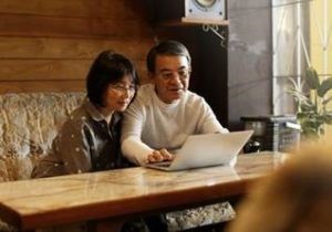 Asian couple at coffee shop looking at laptop together.