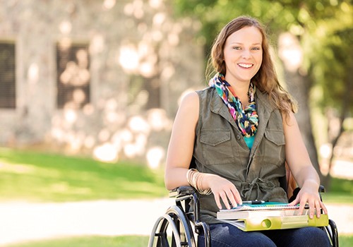 Young woman in wheel chair in foreground and building in the background.