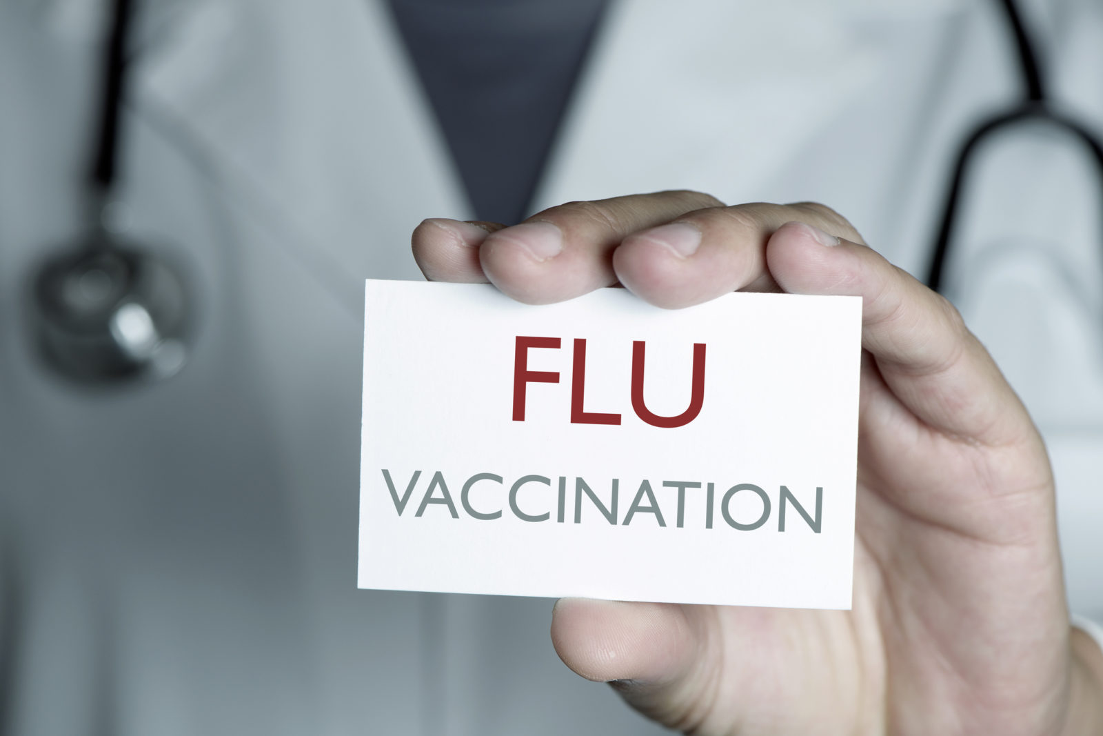 closeup of a young caucasian doctor man in a white coat showing a signboard with the text flu vaccination written in it