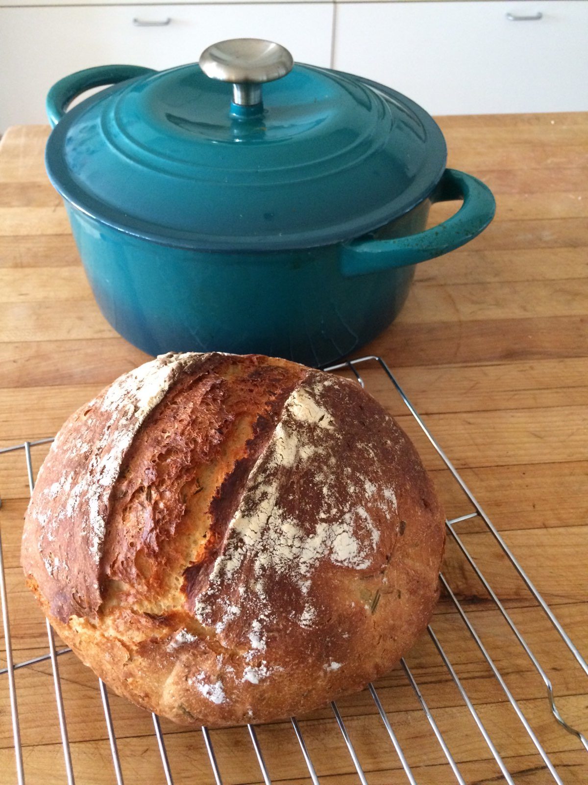 Photo of a round loaf of freshly baked bread next to a blue cast iron casserole dish.