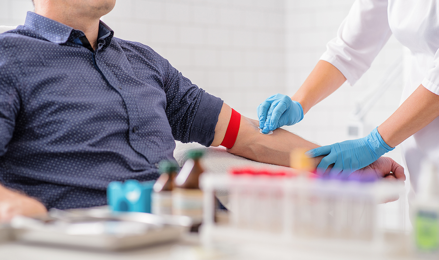 A man waits as a technician cleans his arm prior to a blood draw.
