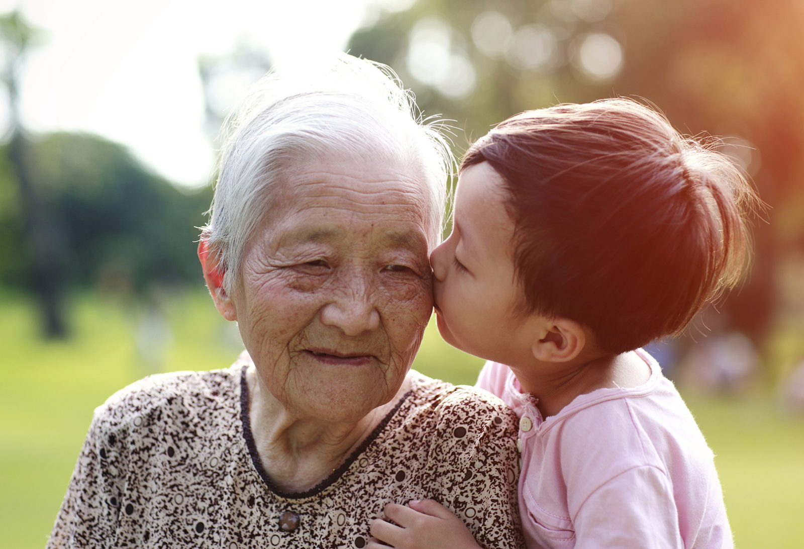 Photo of an older Asian woman and a young child kissing her on the cheek.