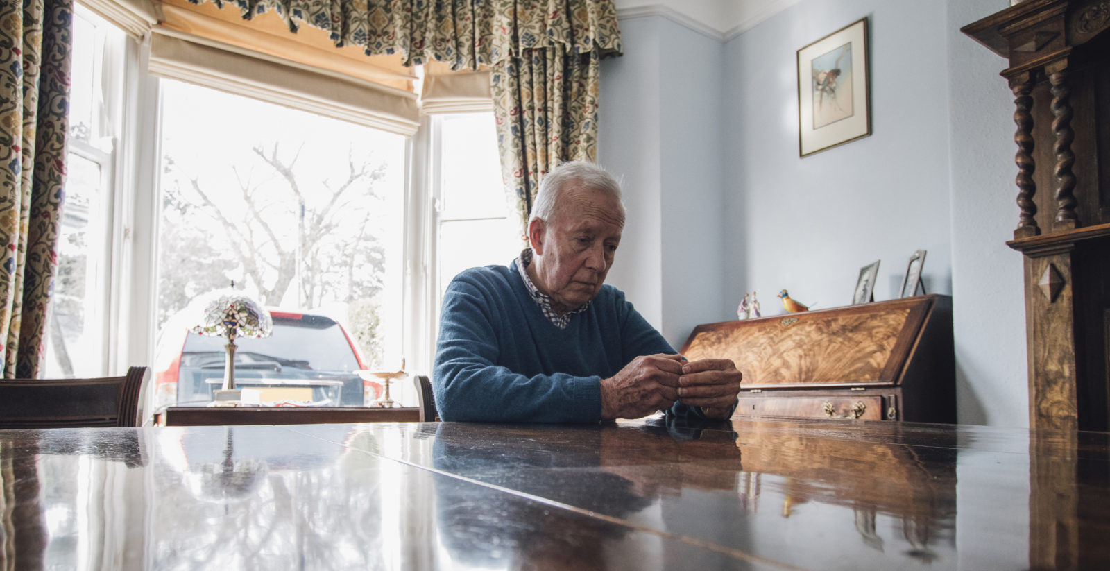 Senior man is sitting alone at the dining table in his home, with a worried expression on his face.