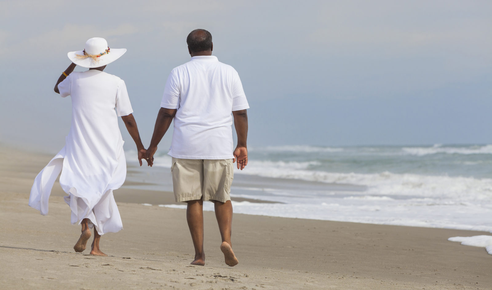 Happy romantic older African American man and woman couple walking holding hands on a deserted tropical beach