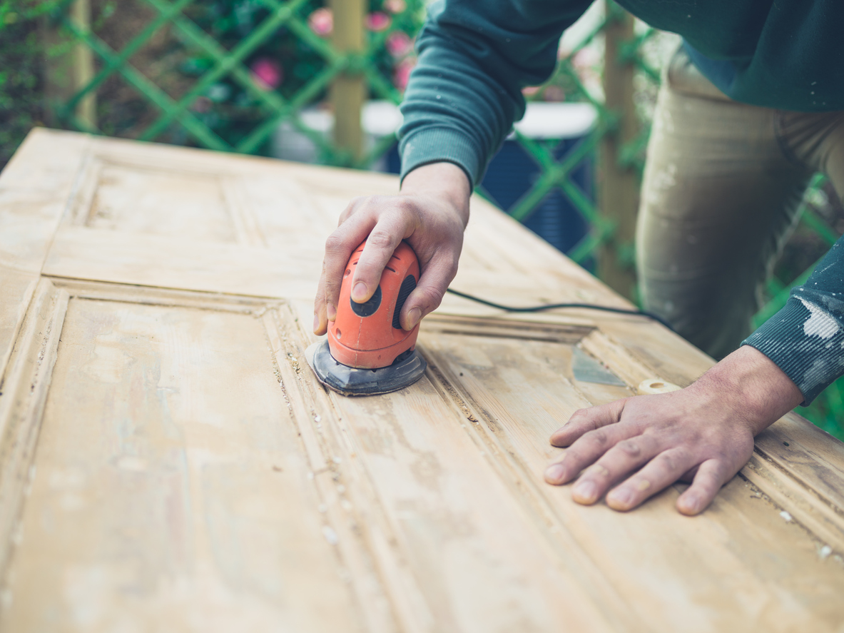 A man is sanding an old door with an electric sander