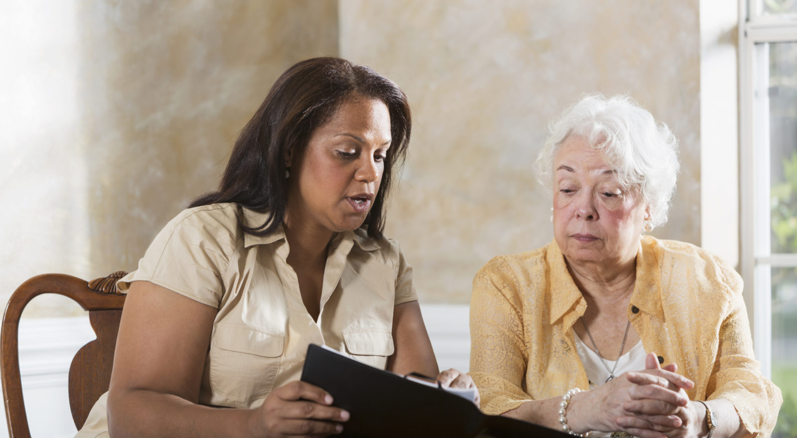 Mature Hispanic woman (50s) advising senior Hispanic woman (70s).
