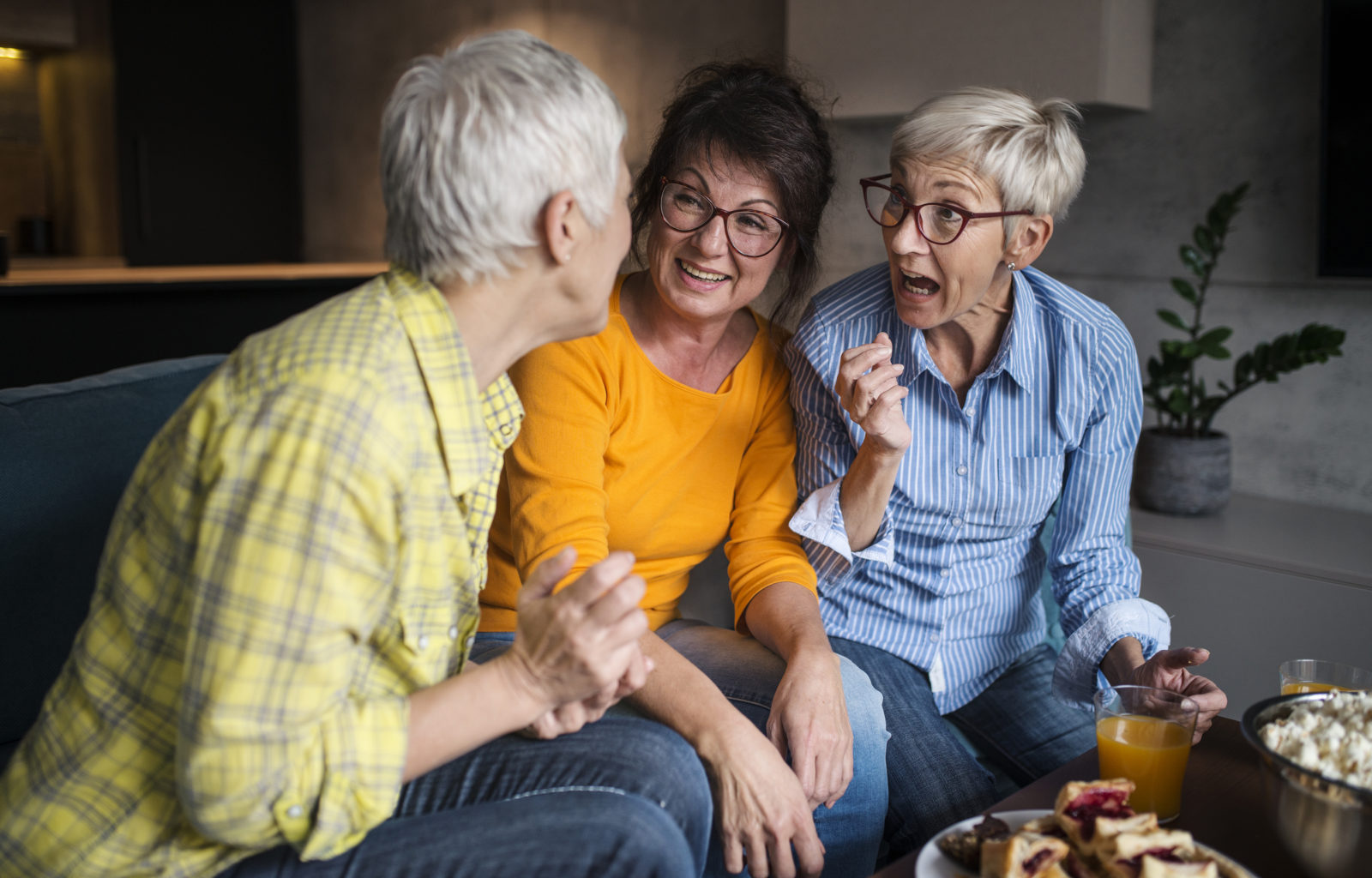 Three older women sitting on a couch, laughing, and enjoying each other's company.