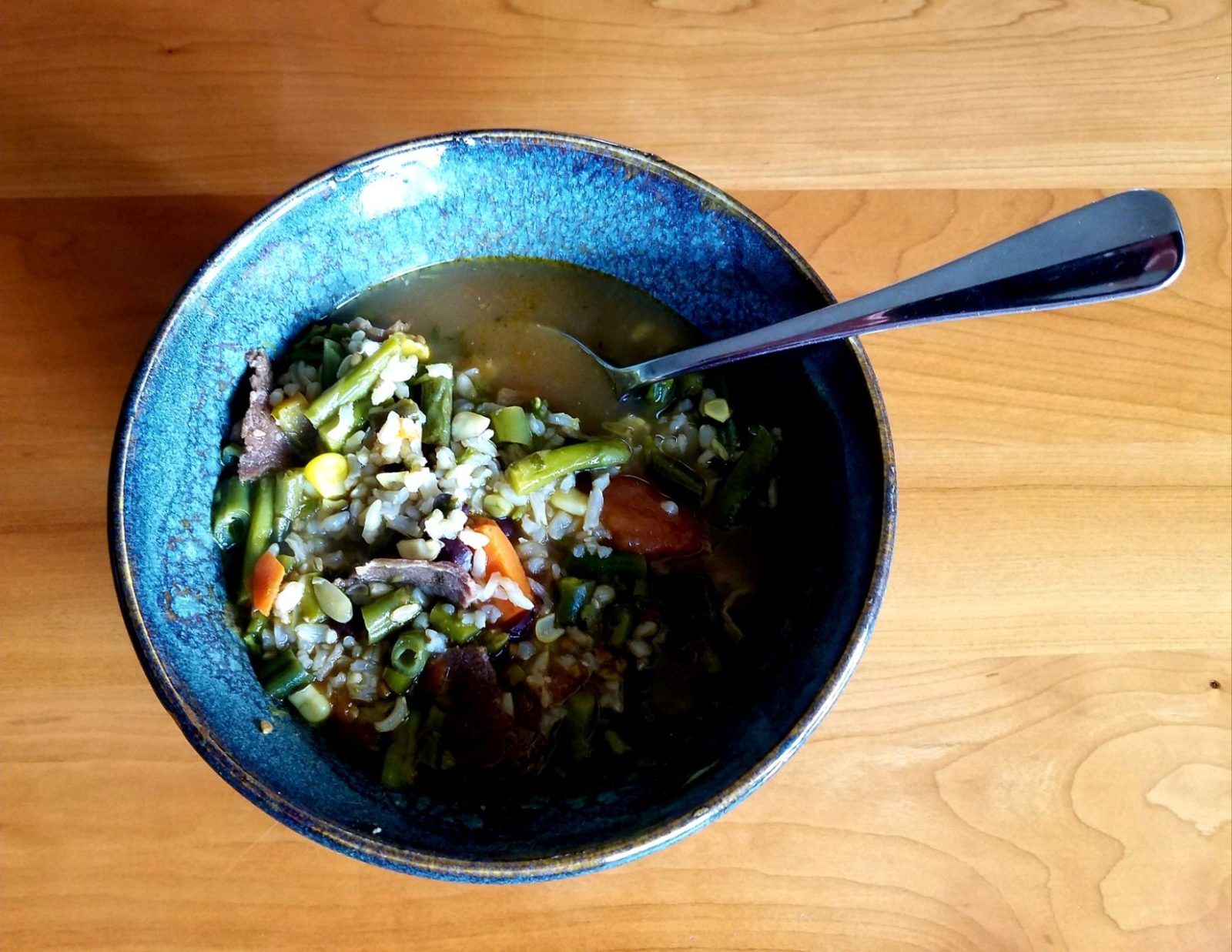 photo of vegetable rice soup in a blue bowl with a spoon on a wooden table