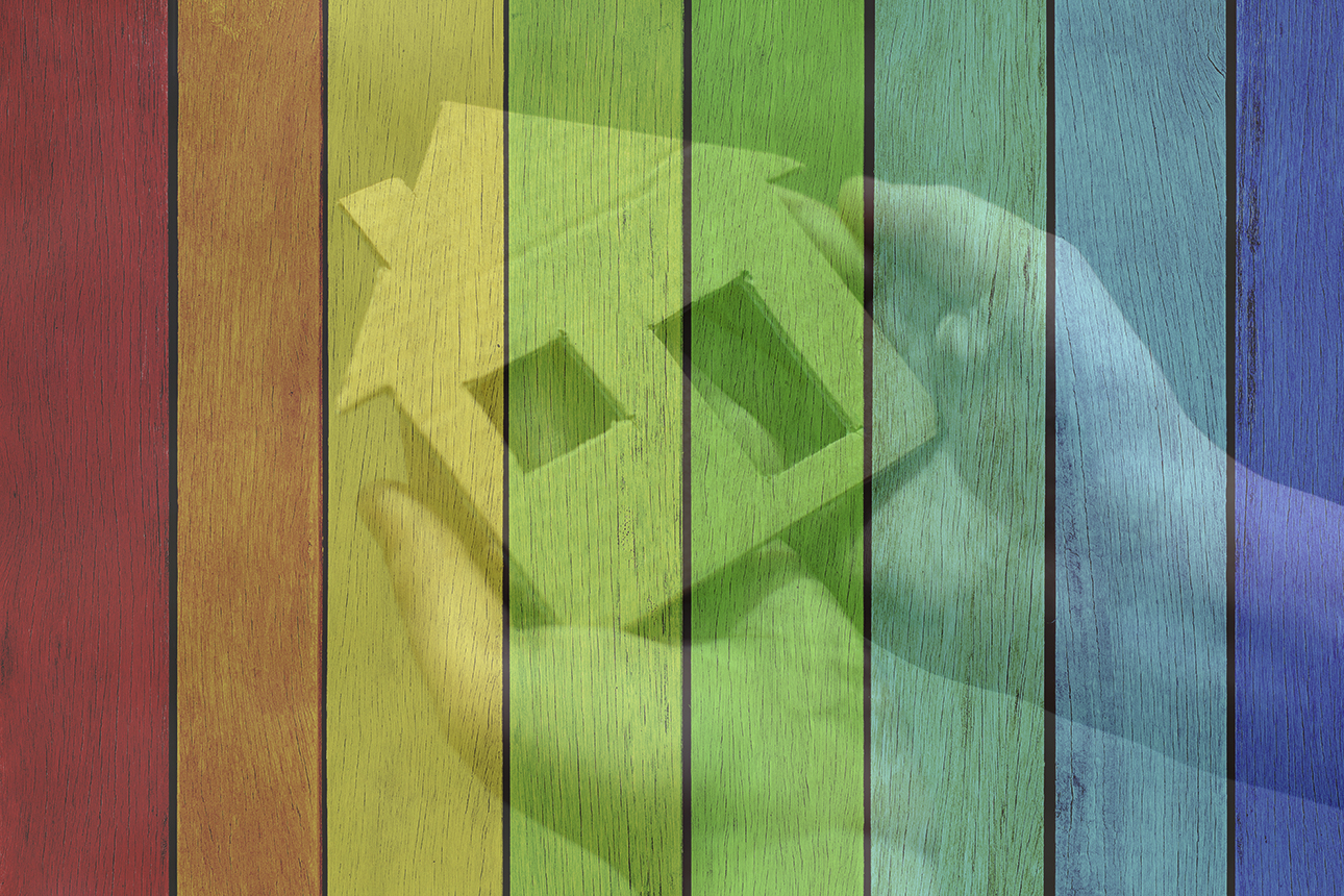 photo of two hands, palms up, holding a cardboard cut-out of a house. The photo includes an overlay of rainbow striped boards.