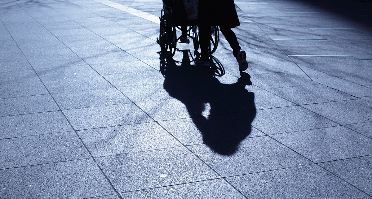 Photo of a sidewalk with the silhouette and shadow of a person walking and pushing a walker.