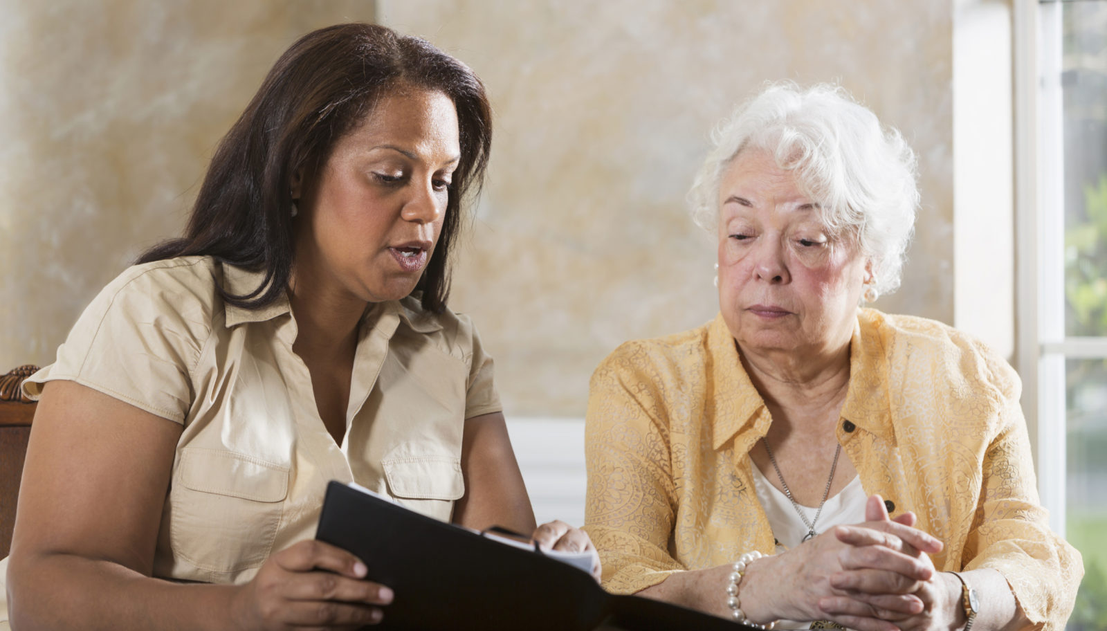 Mature Hispanic woman (50s) advising senior Hispanic woman (70s).
