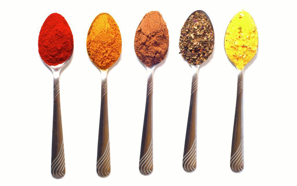 Five spoons, each one holding a different brightly colored spice