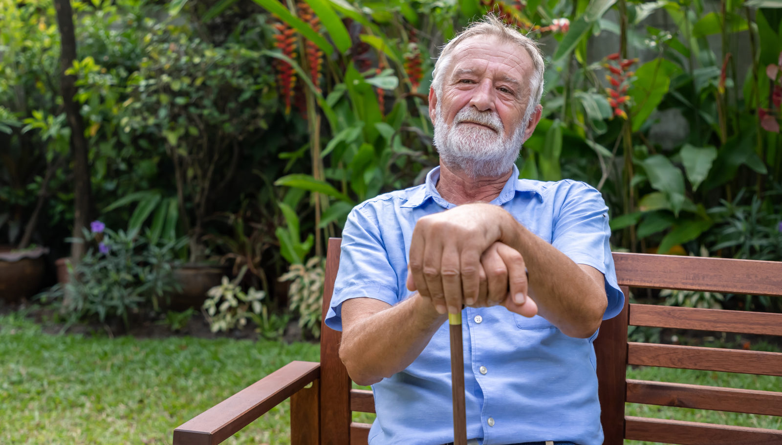 Thoughtful older man holding cane sitting on bench in garden