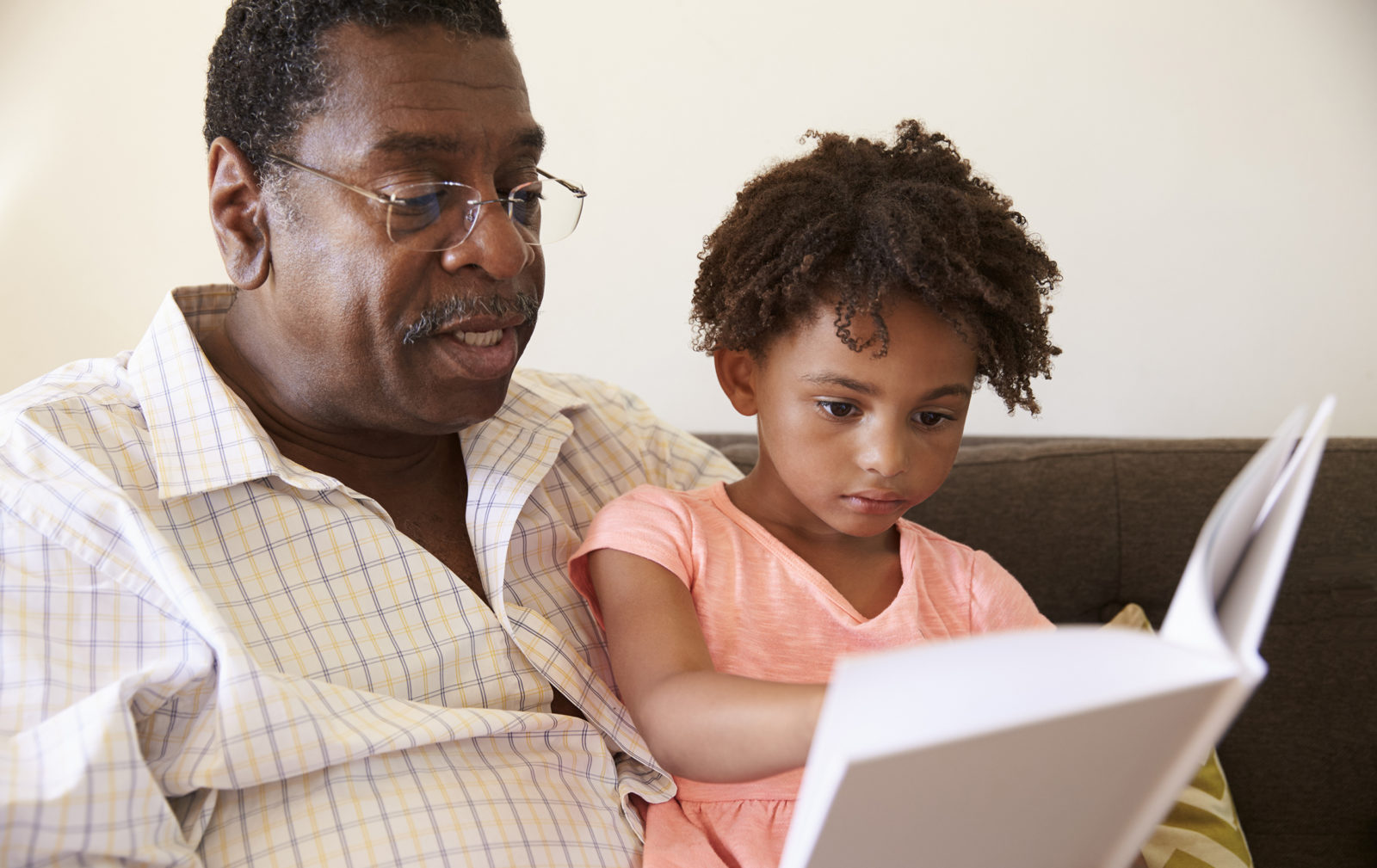 Grandfather And Granddaughter Reading Book At Home Together