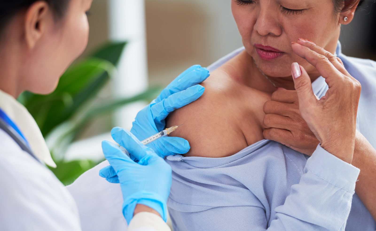 Nurse making injection into shoulder of an older Asian woman