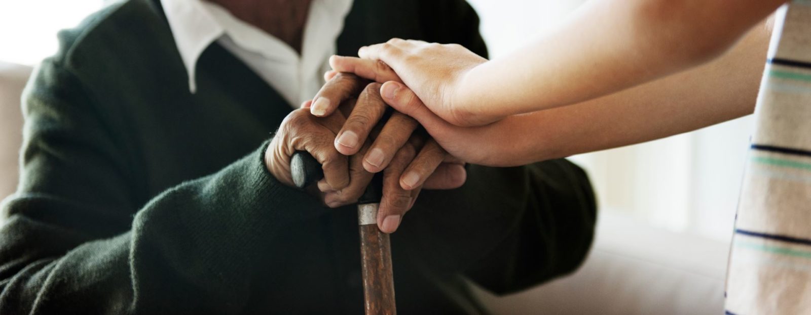 African American male's hands on a cane with smaller hands of a caregiver, providing reassurance
