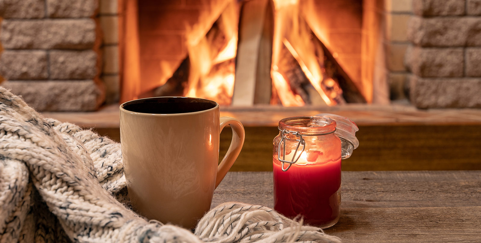 Big mug with hot tea, and a candle , wool scarf, near cozy fireplace