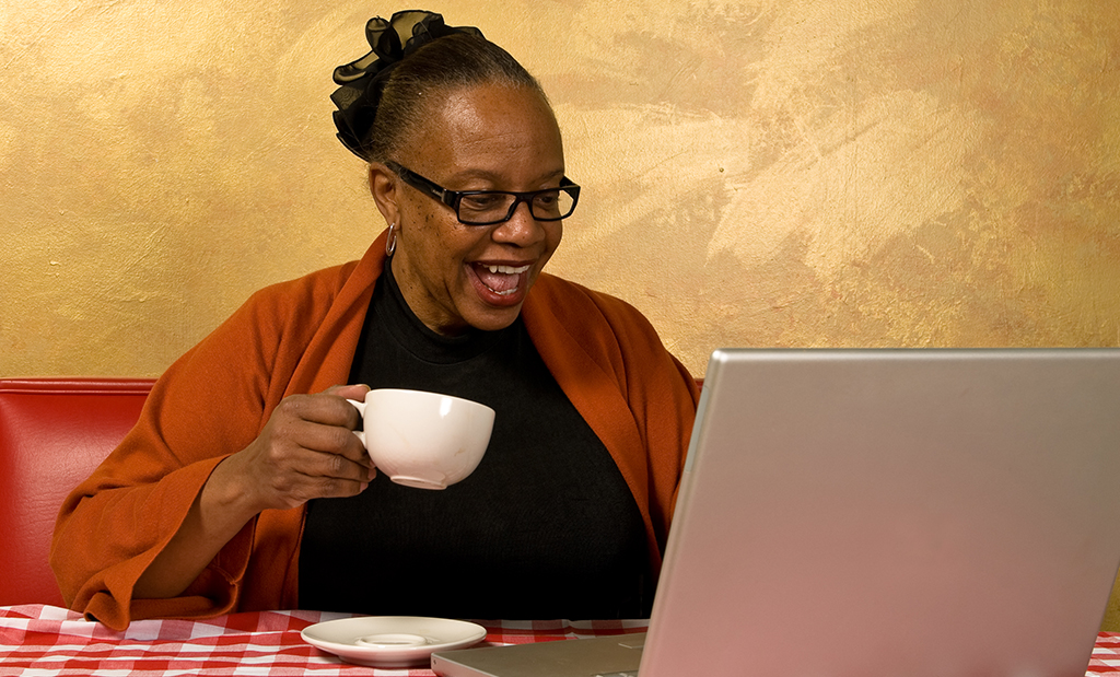 A woman sipping a cup of coffee while using her laptop computer
