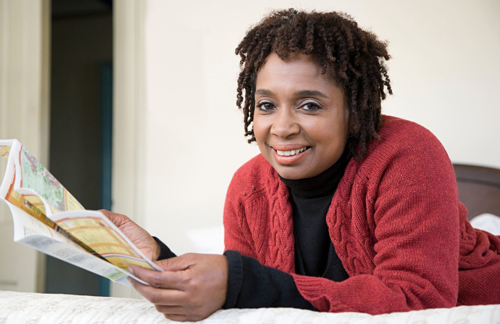 African American woman in a red sweater looks at a map and smiles at the camera