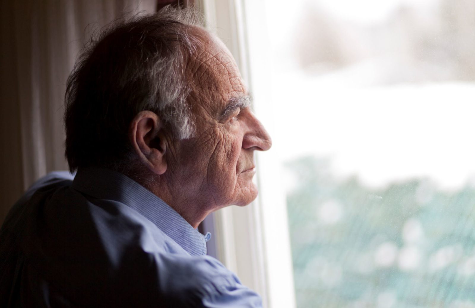 older man looks sad as he gazes out the window