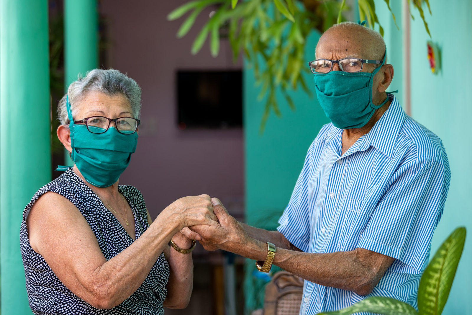 Older woman and man wearing COVID face masks hold their four hands together