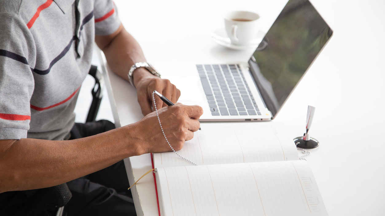 Man's arms and hands, signing a document next to an open laptop computer