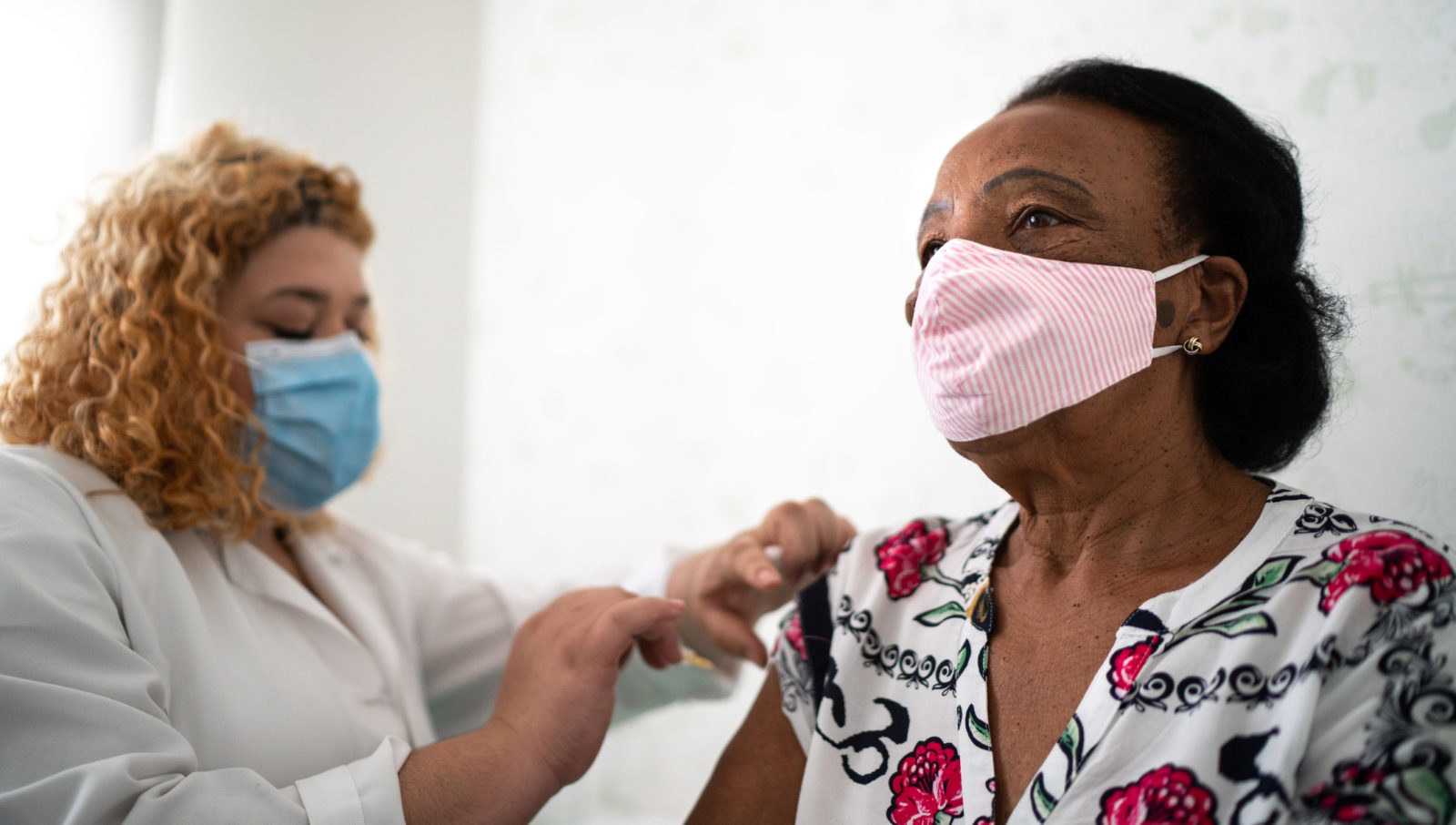 Nurse applying vaccine on patient's arm using face mask