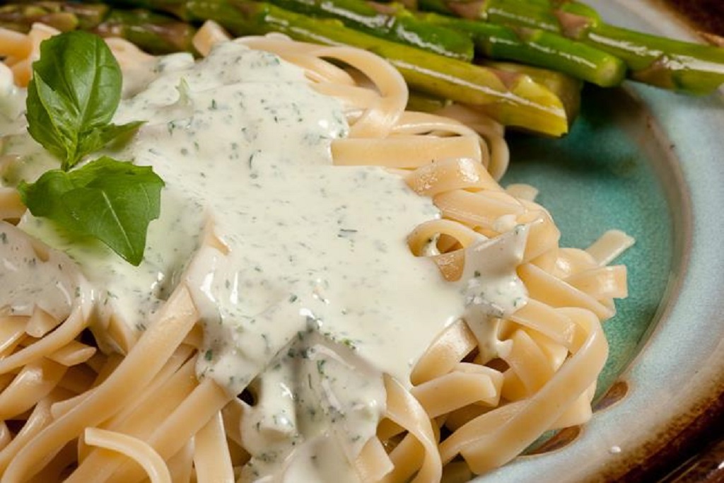 photo of fettuccine alfredo on a dinner plate with asparagus and a sprig of basil