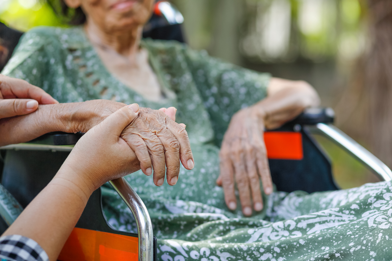 Older woman on wheelchair at home with caregiver's hand