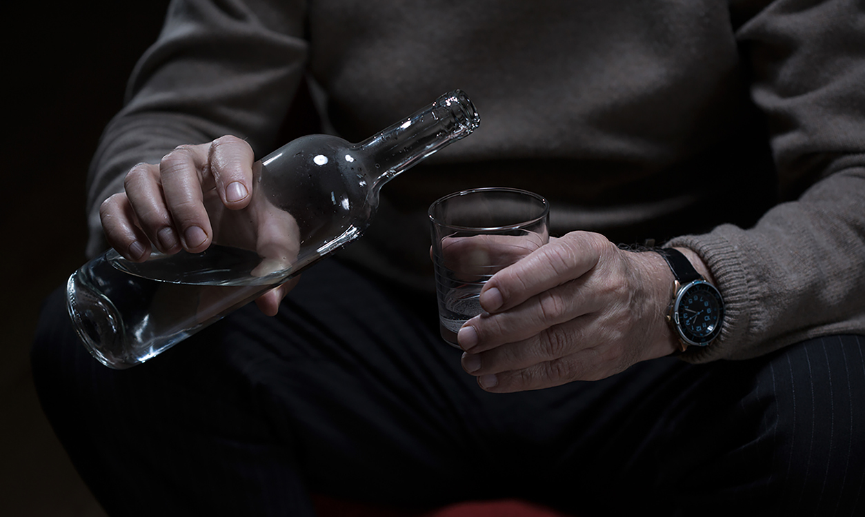 Close-up to male hand holding glass and bottle of alcohol