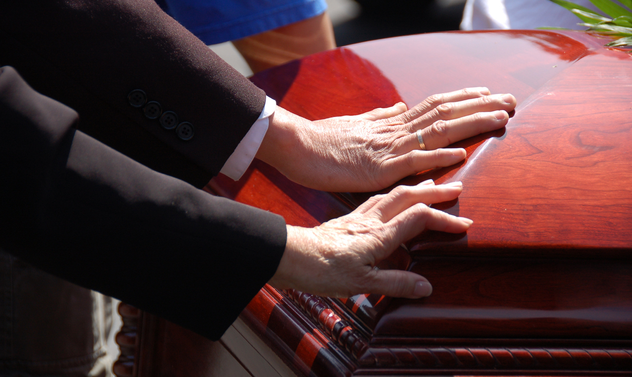 2 hands touching a closed wooden casket. Farewell to a loved one.