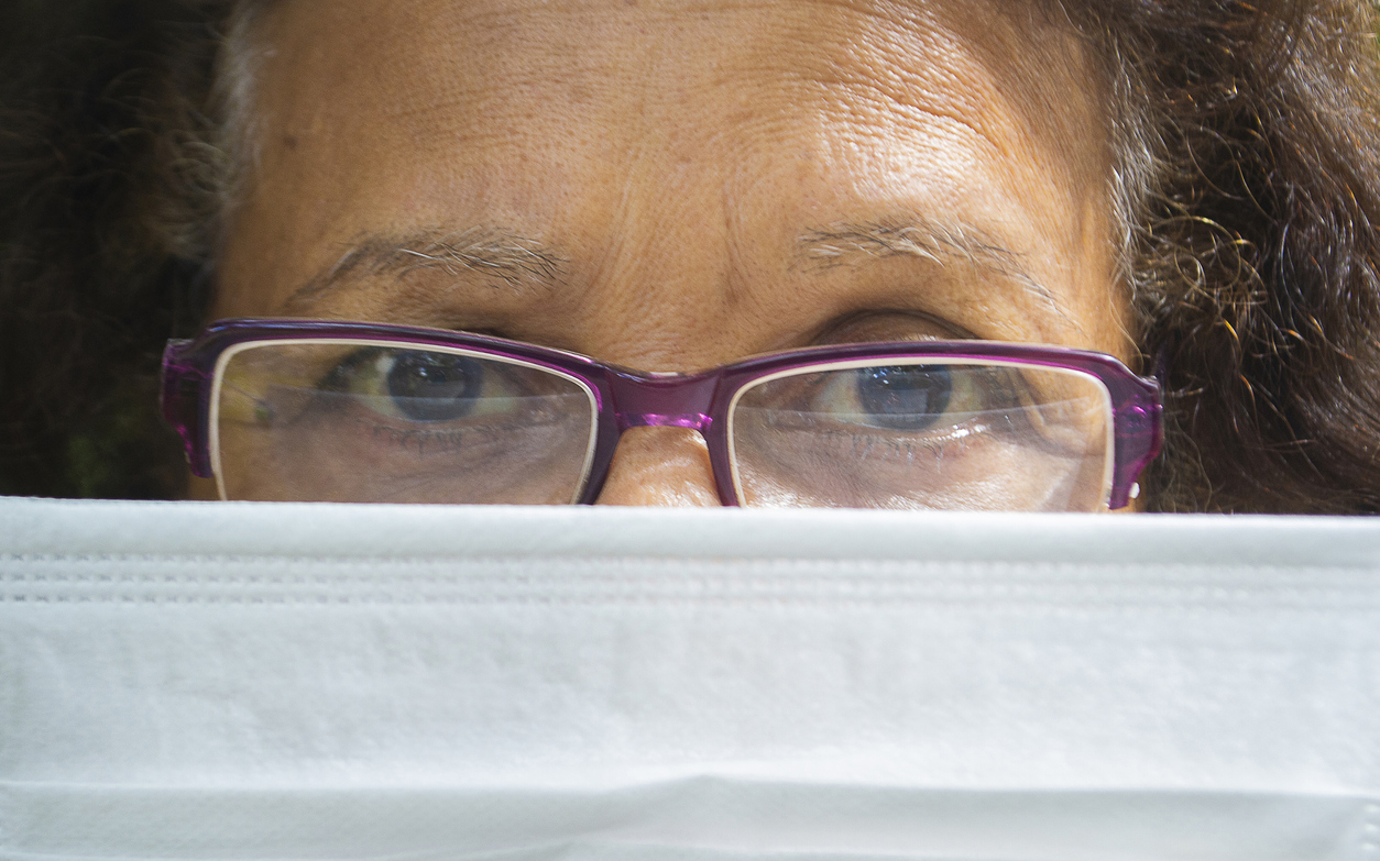 photo of older woman with glasses, peering over the top of an outstretched white medical mask