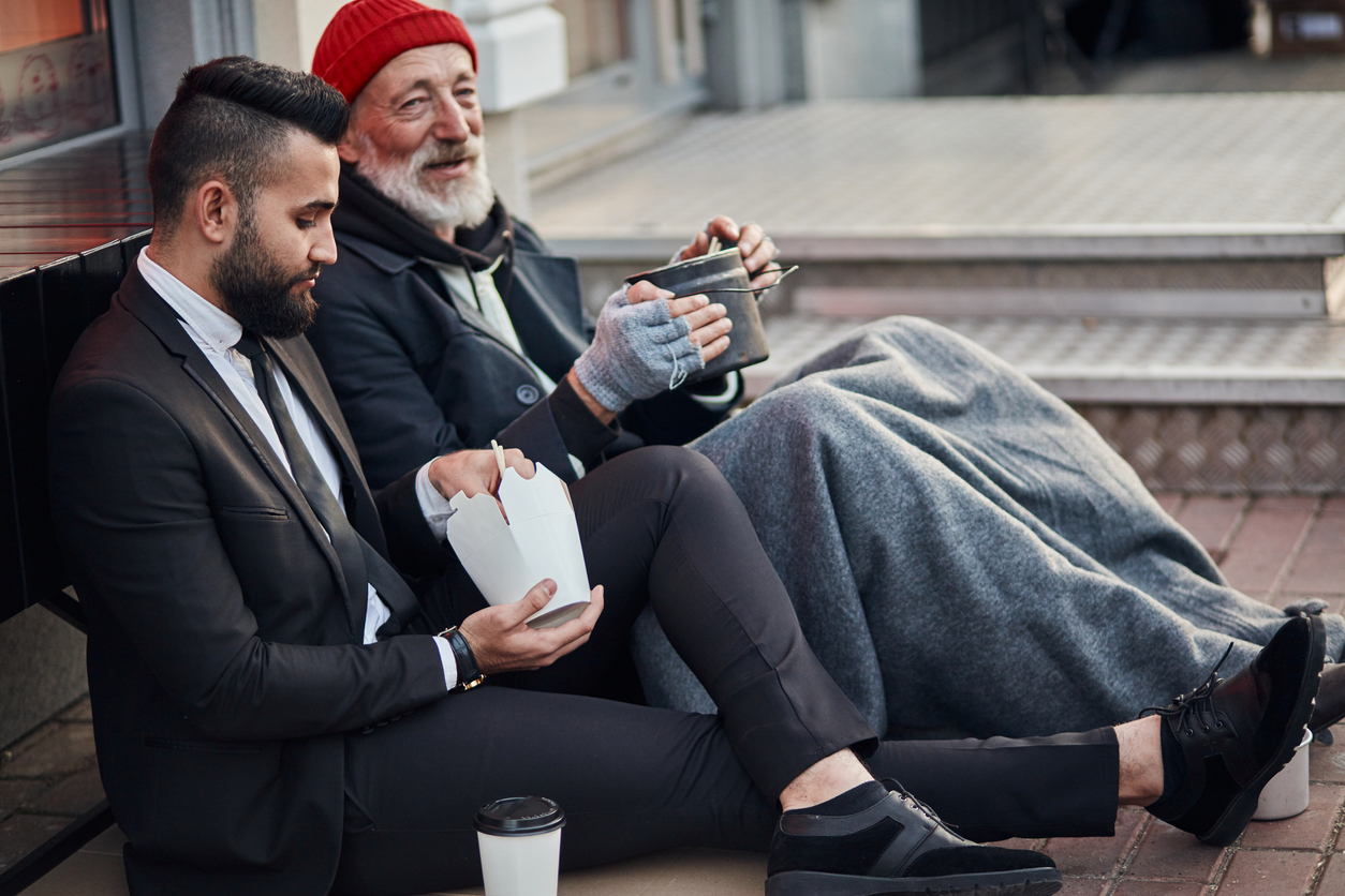 businessman in suit sitting on floor with homeless man, listening his story