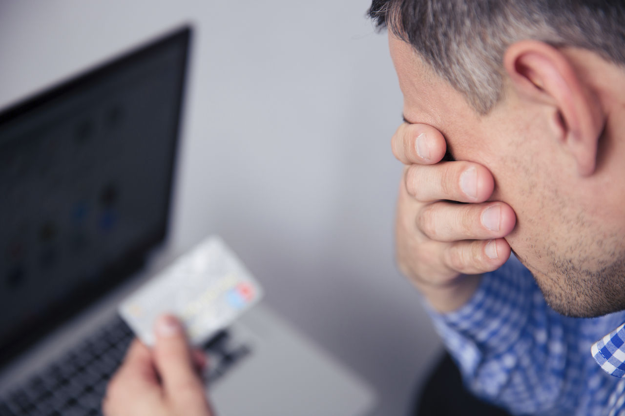 man looking distressed at a credit card and laptop computer