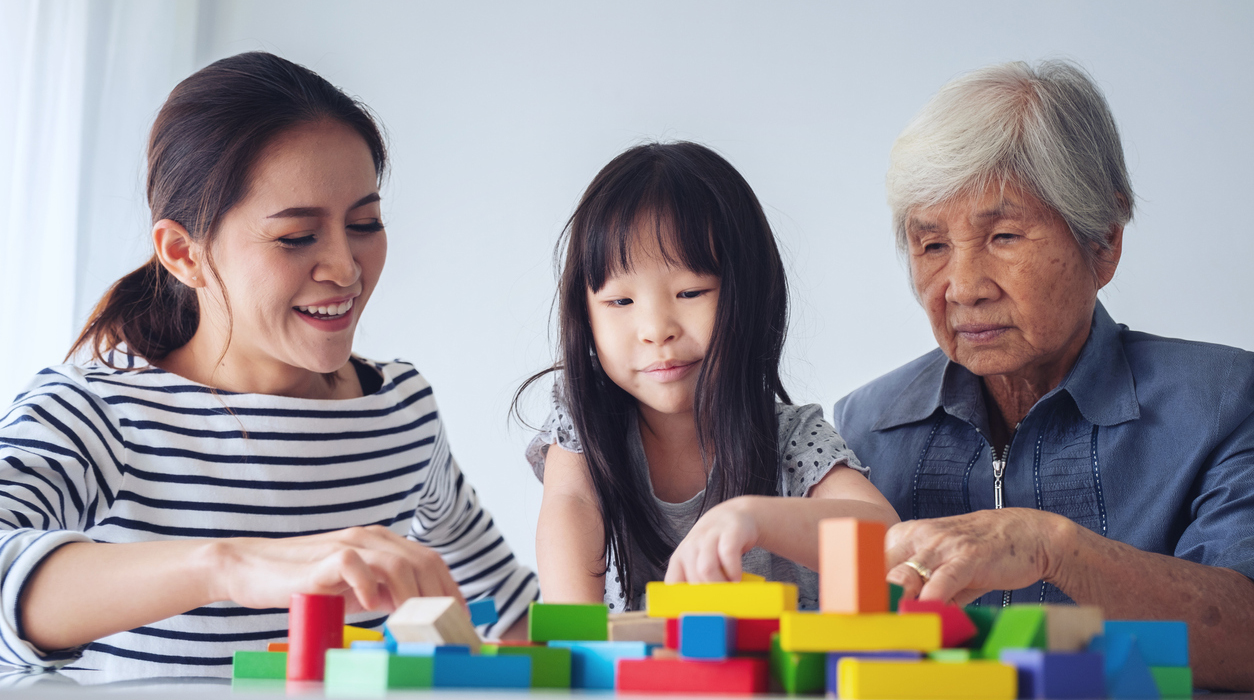 Mother, child, and grandmother work together with colorful play blocks