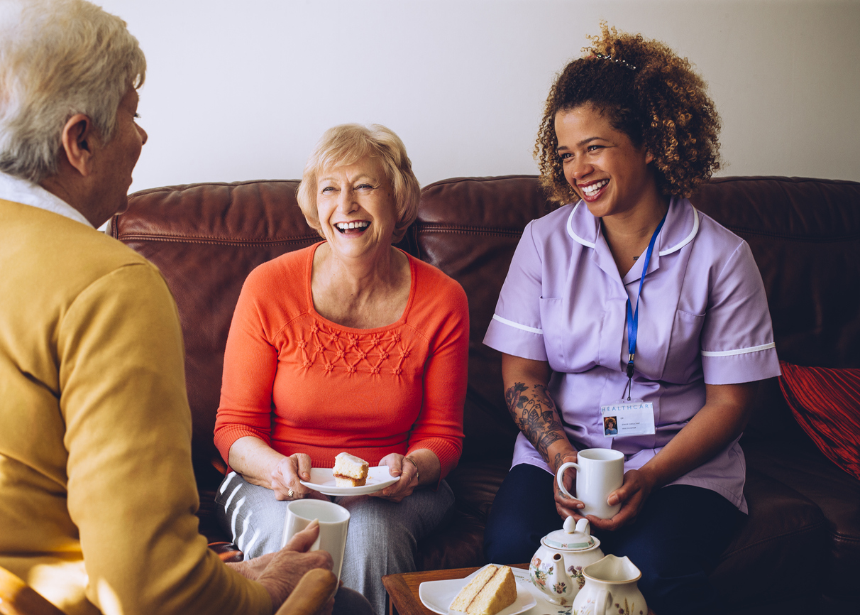 three women, one a caregiver, enjoying coffee and conversation in a care setting