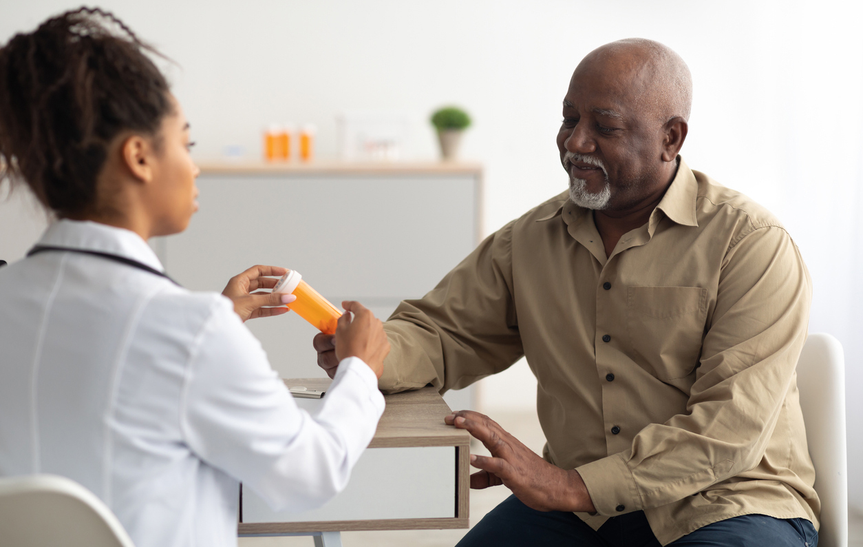 older African American man accept prescription container from a younger African American health care professional