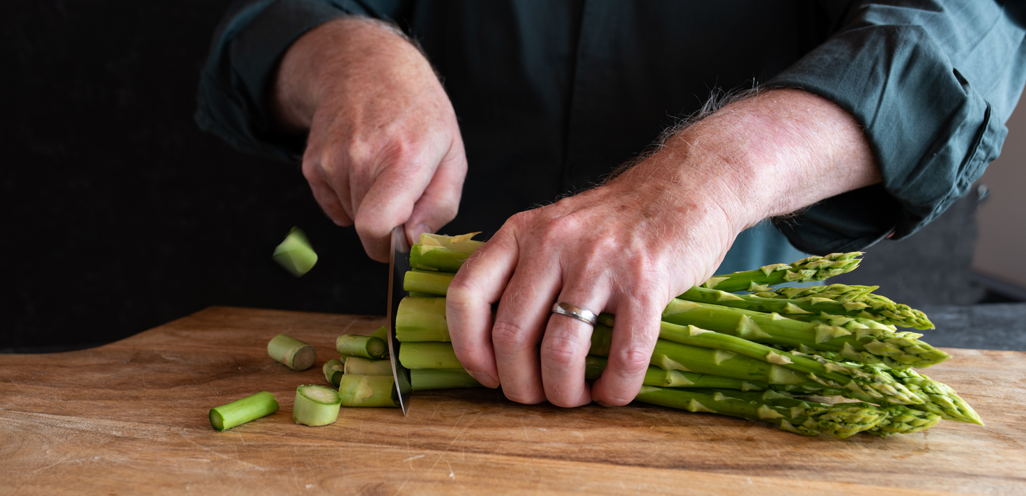 Hands cutting green asparagus on a wooden cutting board