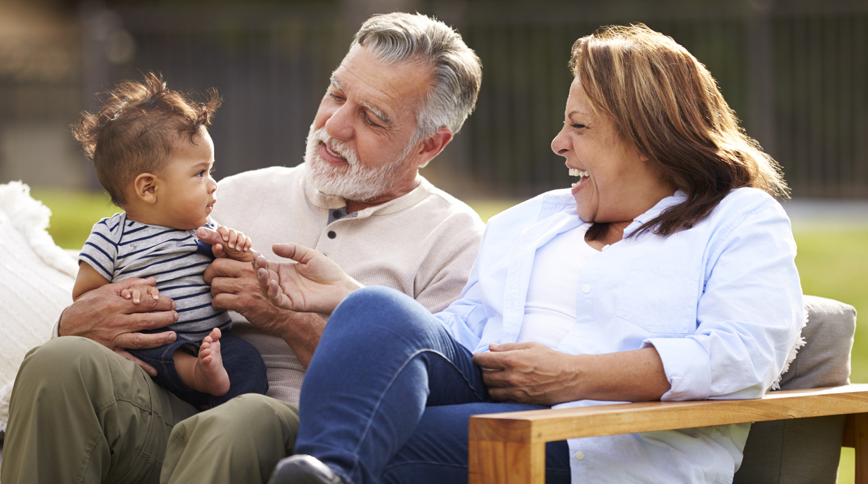 Older couple sitting in the garden with their baby grandson, smiling at him