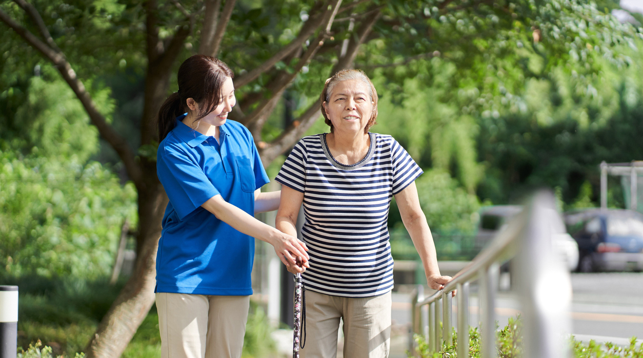 Older woman walking with the help of a caregiver and a walker