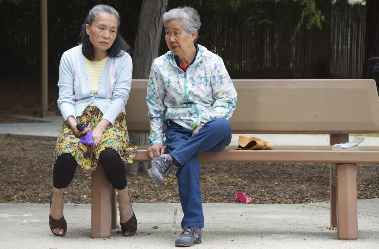 2 Asian women sitting and talking on a park bench