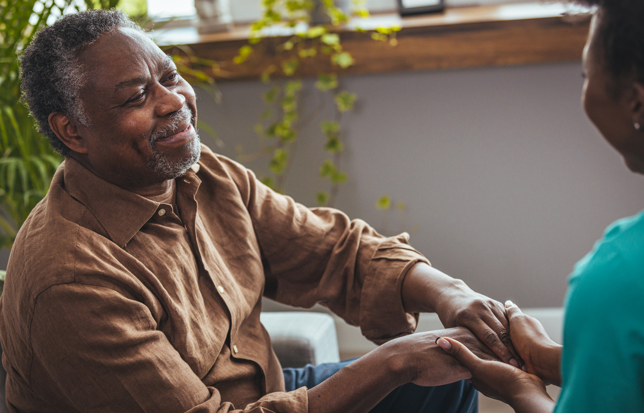 Older man of African descent smiles and holds hands with his female caregiver